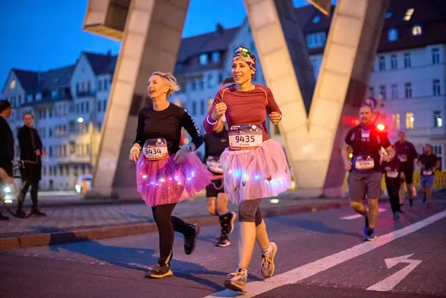 Läuferinnen laufen mit leuchtenden Kostümen durch das Doppel M