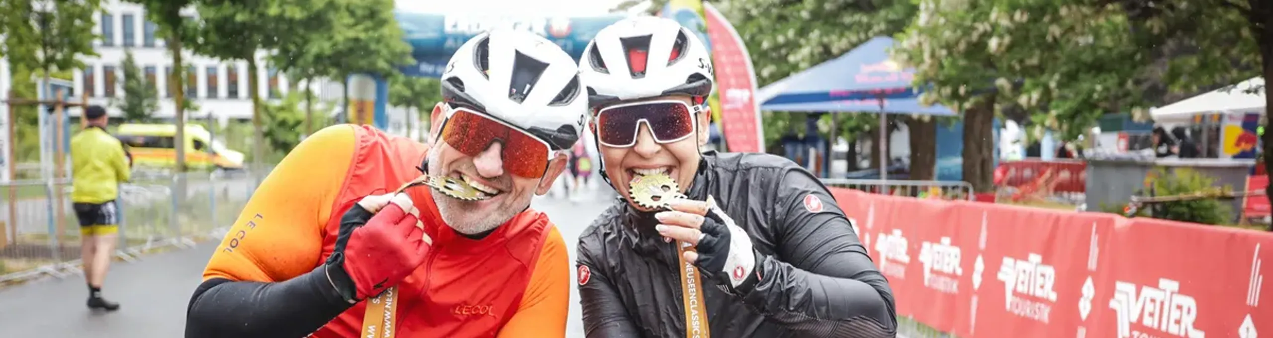 Zwei Rennradfahrer beißen auf ihre Finisher-Medaillen