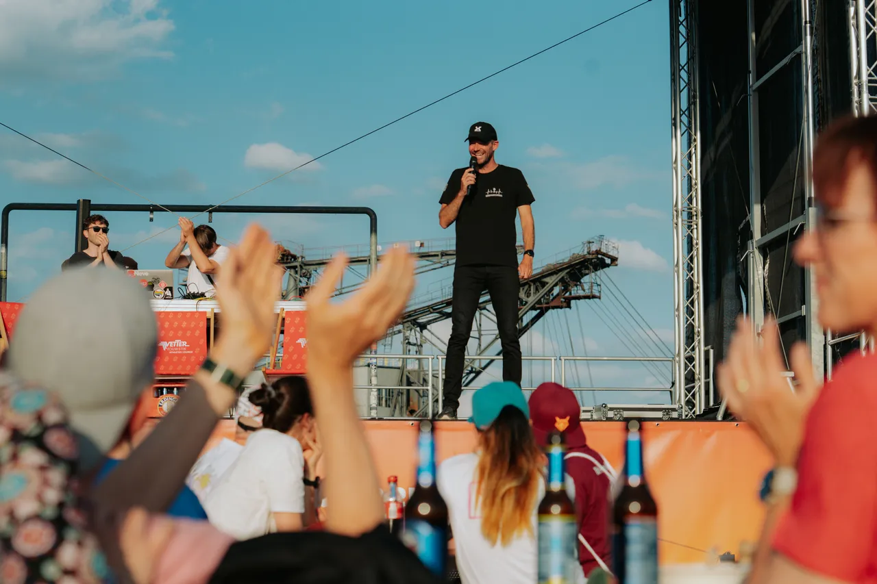 Sven Körbs moderiert auf einer Bühne vor feiernden Menschen