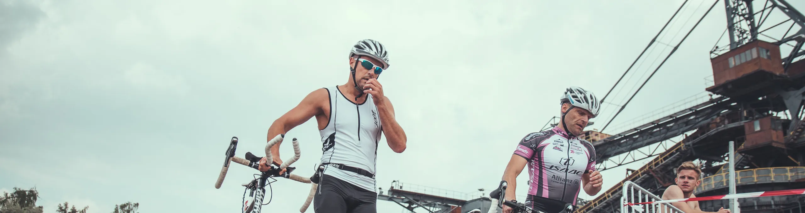 Zwei Radfahrer schieben ihr Rad vor der Kulisse von Ferropolis